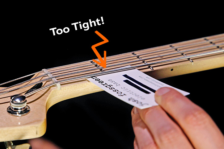 Picture showing a bass with strings tightened under which a business card does not fit